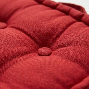 Close-up of red tufted upholstery with a central fabric button on a cushioned surface.